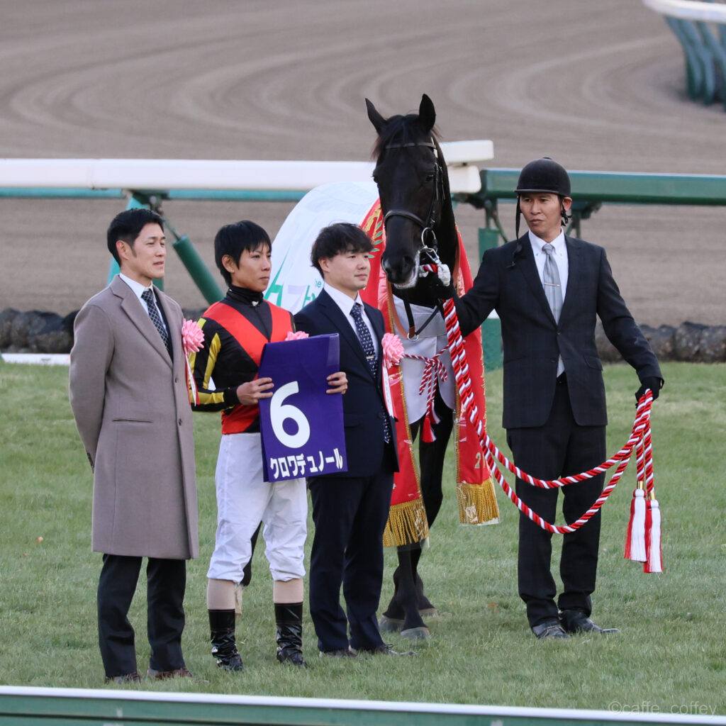 ホープフルステークス優勝後、クロワデュノールと斉藤調教師・北村騎手・厩舎陣営が並ぶ口取り写真。チームの絆が感じられる勝利の記念