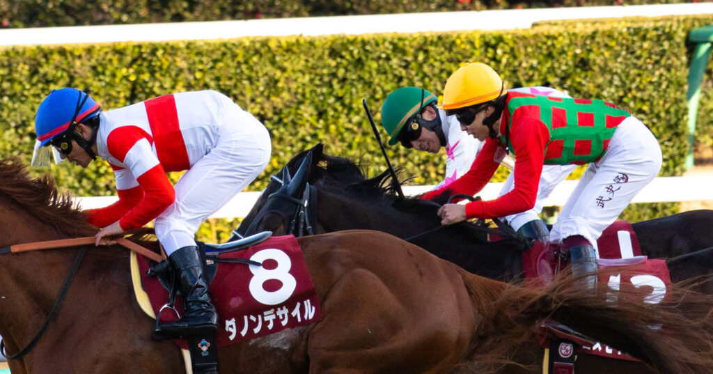 2025年撮影、中山競馬場で行われたAJCC（アメリカジョッキークラブカップ）のゴール前接戦で、外から差し切ったダノンデサイルの勝利を見届けた横山典弘騎手が笑顔を見せる。コスモキュランダの横山武史騎手も微笑む親子騎手の貴重なワンシーン