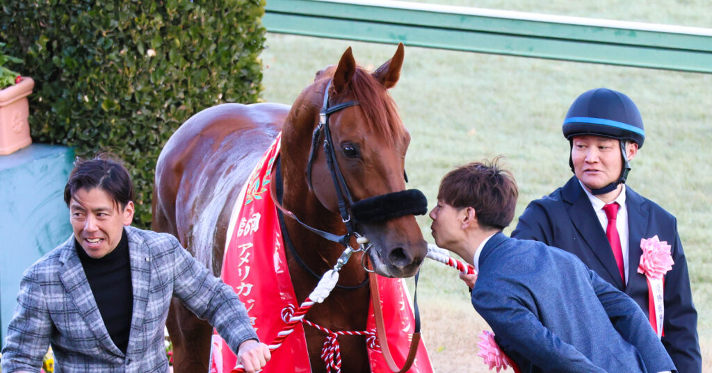 AJCC優勝後のウイナーズサークルで、愛馬ダノンデサイルにキスするように顔を近づける安田翔伍調教師。一方で少し戸惑った表情のダノンデサイルが微笑ましい、2025年1月26日の中山競馬場での表彰式シーン