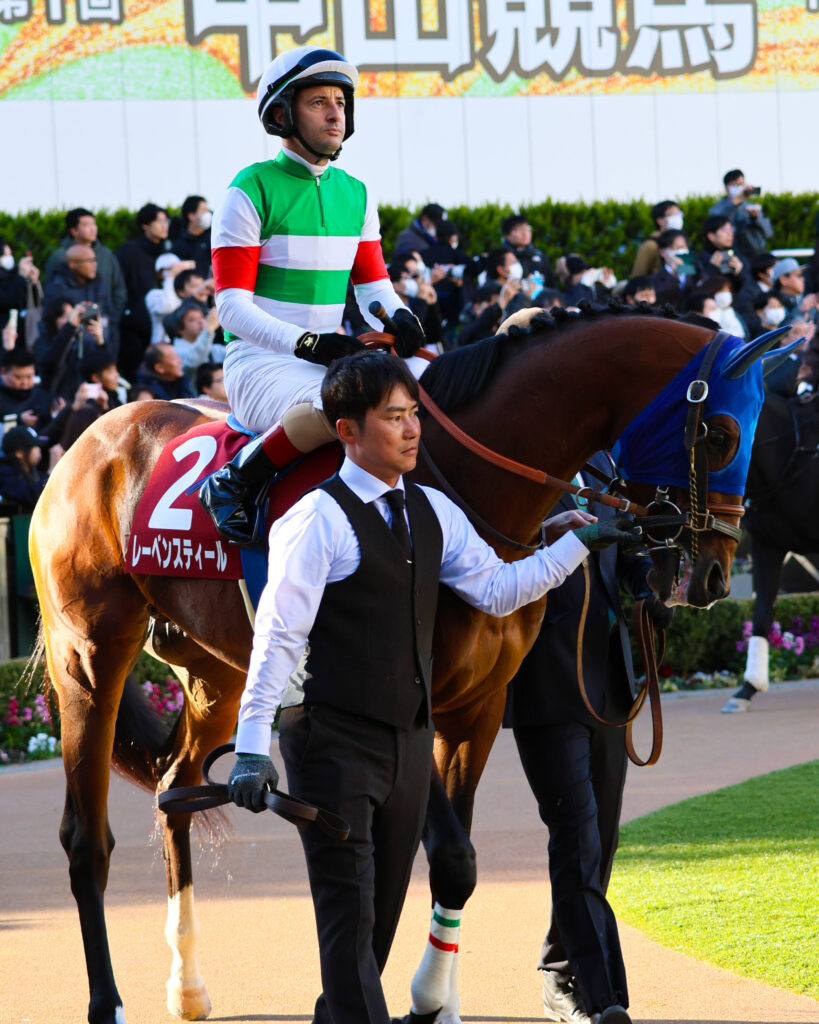 2025年撮影、中山競馬場で行われたアメリカジョッキークラブカップのパドックに登場したレーベンスティール。クリストフ・ルメール騎手を背に、風格ある佇まいを見せた写真