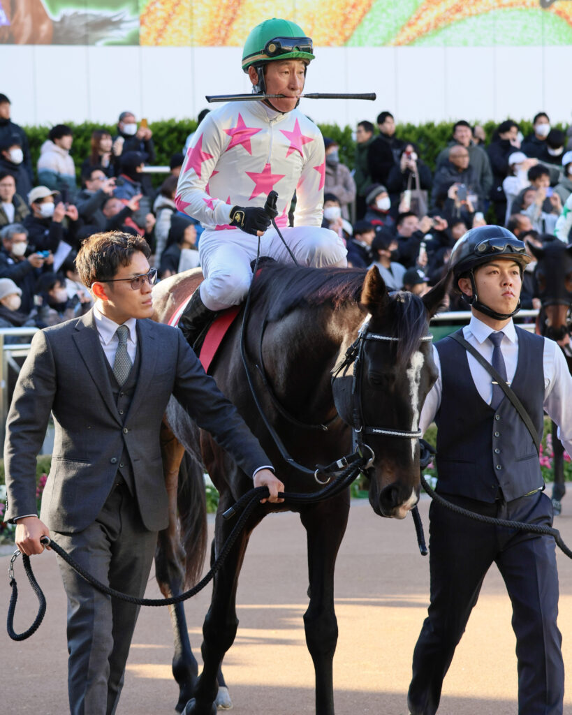 AJCCのパドックで、横山典弘騎手が咥えムチの姿で騎乗するマテンロウレオ。2025年1月26日、中山競馬場で撮影された、騎手の個性と馬の落ち着きが感じられる一枚