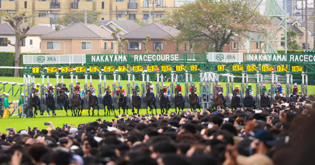2025年4月20日、中山競馬場で行われた皐月賞のスタート直後、ゲートが開いて各馬が揃って飛び出す緊張感あふれる瞬間を捉えた写真
