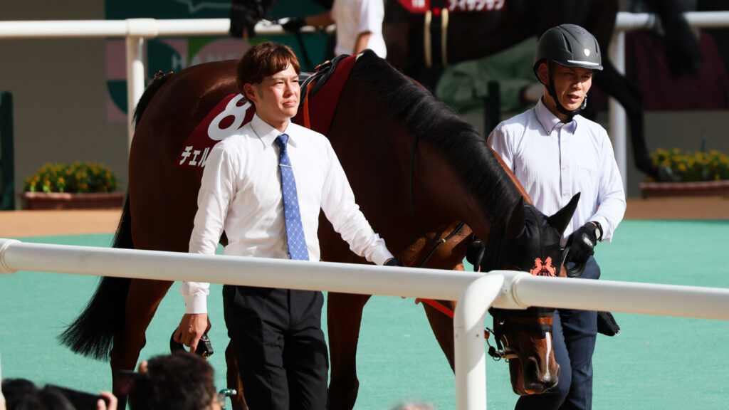GⅡローズステークス当日、阪神競馬場のパドックを二人引きで歩くチェルビアット。首を下げて地面を見るようなウシュバスタイルで歩いている。