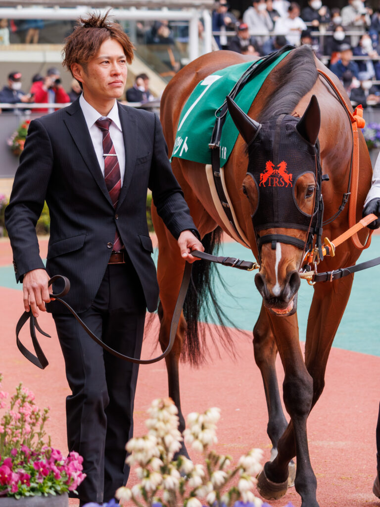 2026年3月22日、中京競馬場の愛知杯パドックを周回するチェルビアット。外周の花に目を向けるようなかわいらしい表情が印象的な一枚。